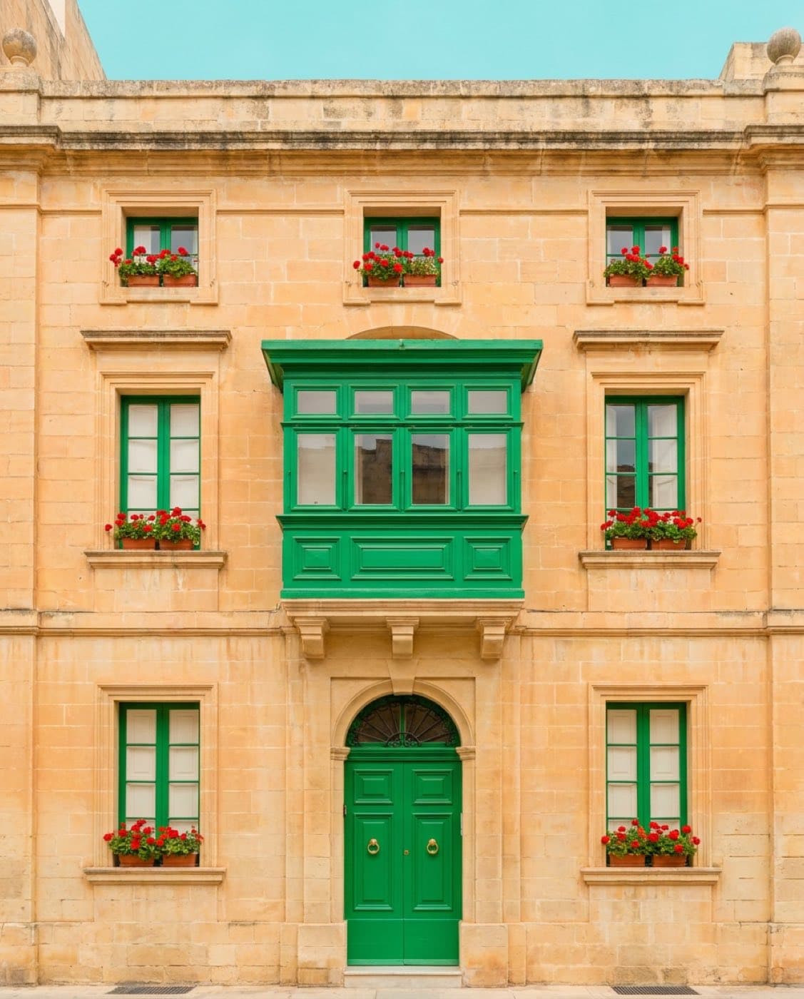 Casa Perellos, Valletta — a symmetrical honey-limestone facade with a green closed balcony, photographed frontally in soft pastel light