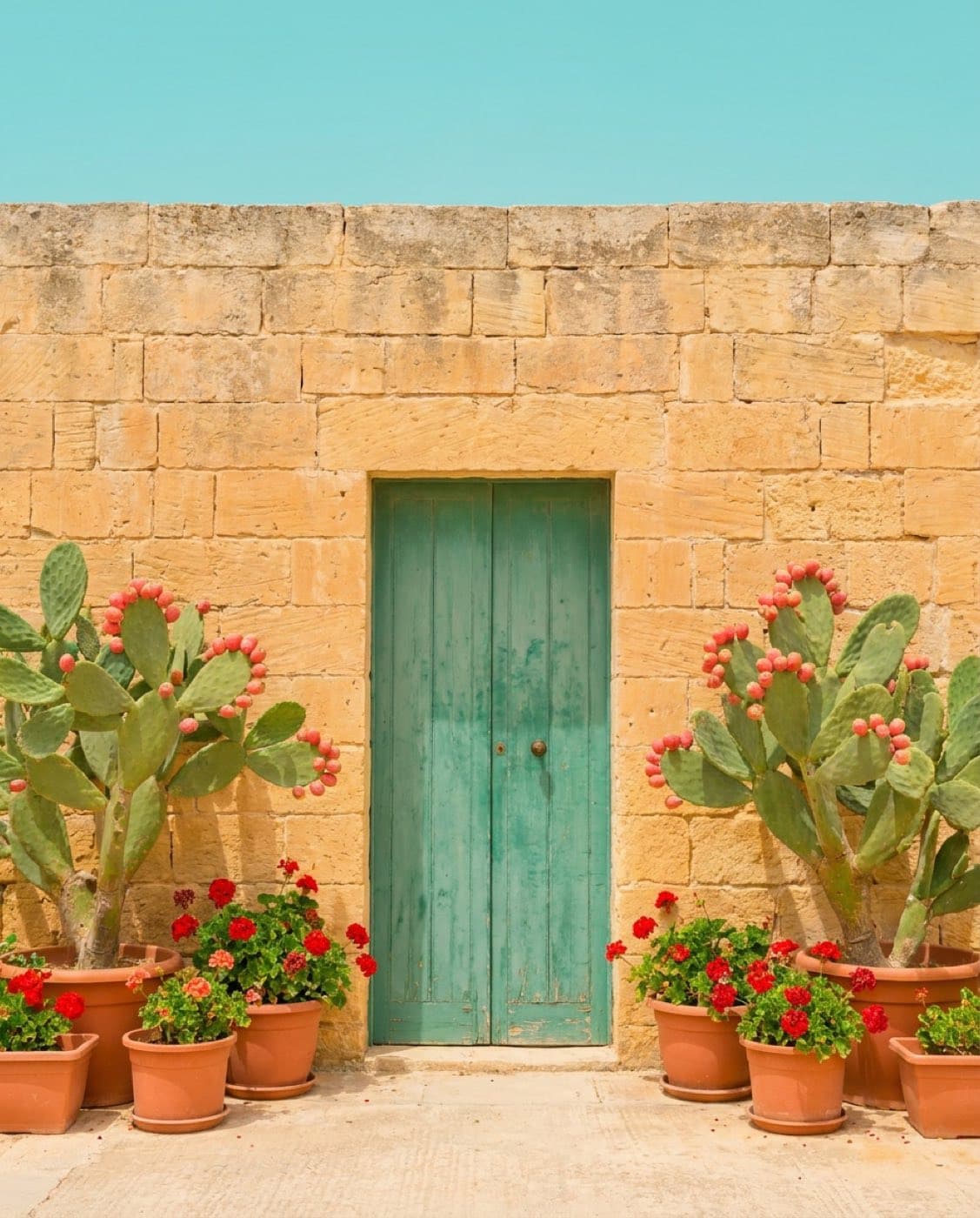 Ta' Lellux, Għarb — a rustic Gozo farmhouse of rough limestone with a weathered green door, centered, under a pastel sky